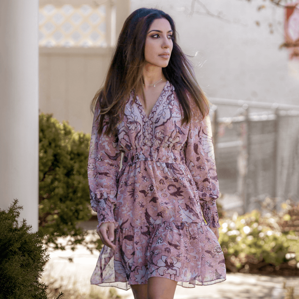 Frau in einem floral gemusterten Kleid mit langen Ärmeln, lächelnd auf einem Gehweg im Freien.