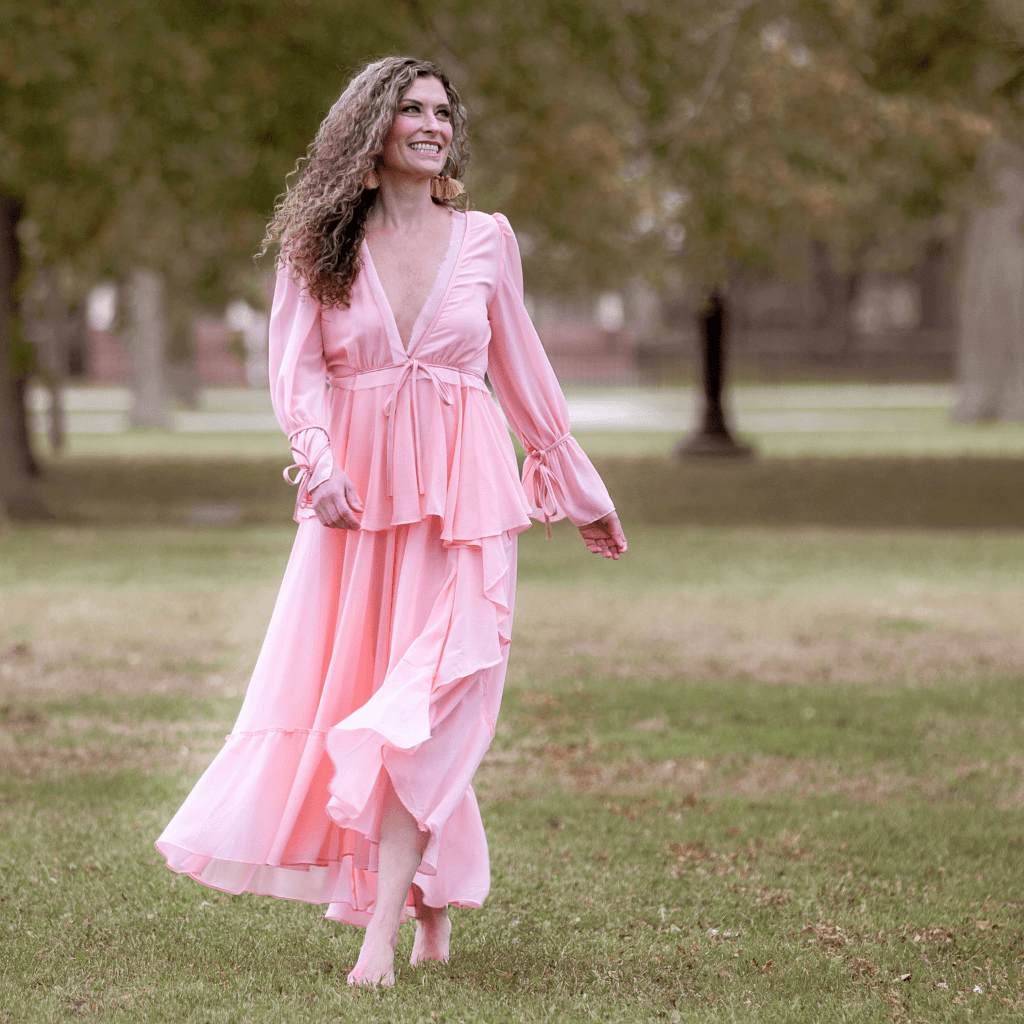 Frau in einem fließenden rosa Kleid, das in einem Park läuft, umgeben von Bäumen und Natur.
