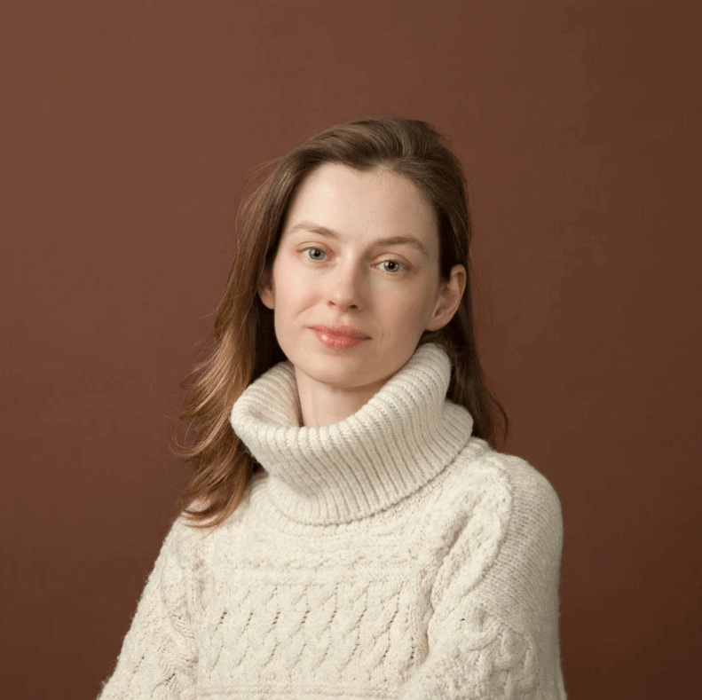 Portrait of a woman wearing a cozy white sweater against a brown background.