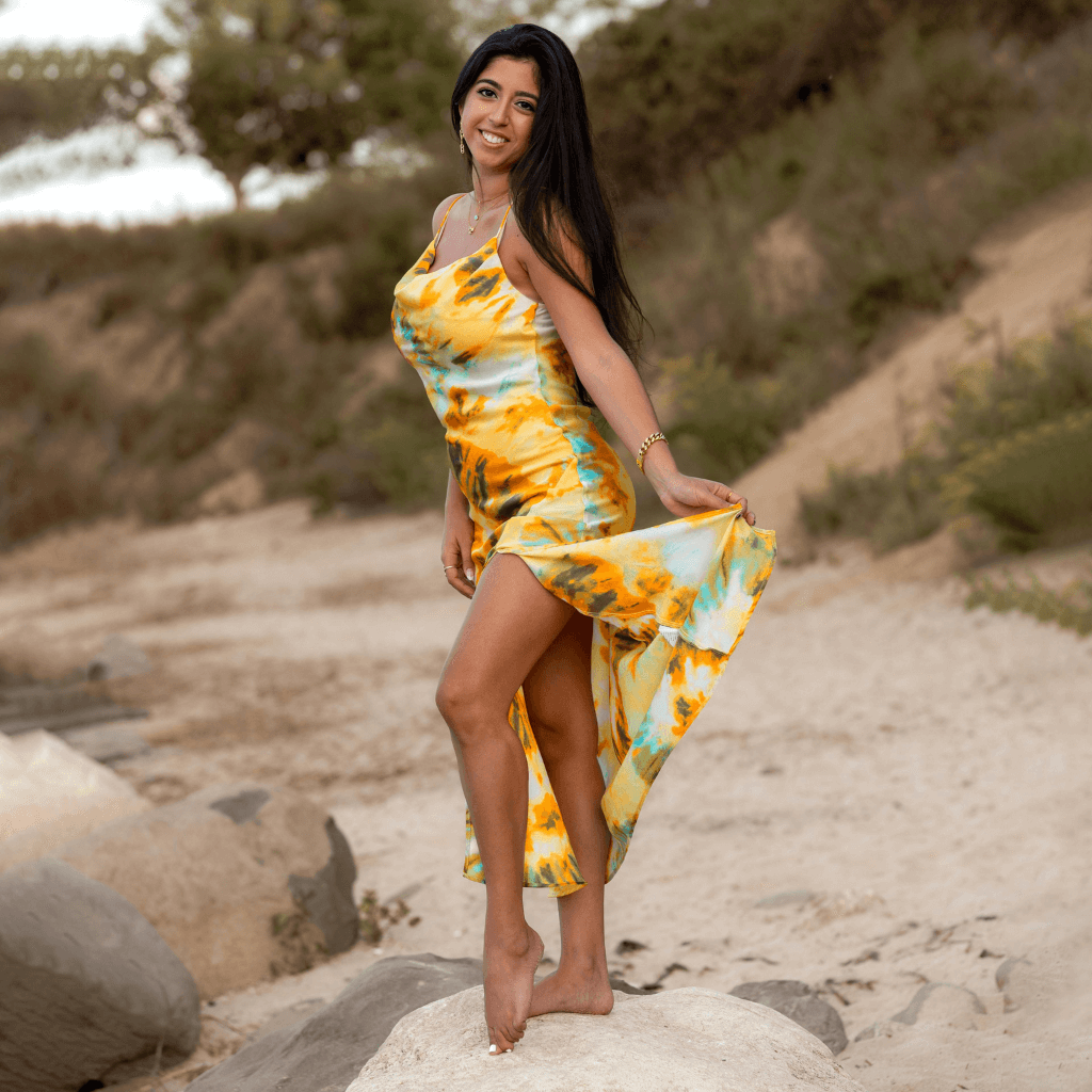 Frau in einem bunten, leichten Sommerkleid mit hohem Schlitz, posiert am Strand.